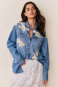 Woman wearing Blue denim shirt with floral lace embroidery and white skirt on a beige background