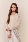 Young girl wearing a cream cardigan over a striped dress against a beige background