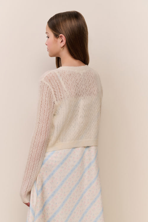 Girl wearing a beige knitted cardigan with ruffles on a plain background