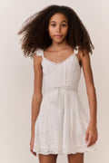 Tween girl wearing a white lace sleeveless dress against a plain background