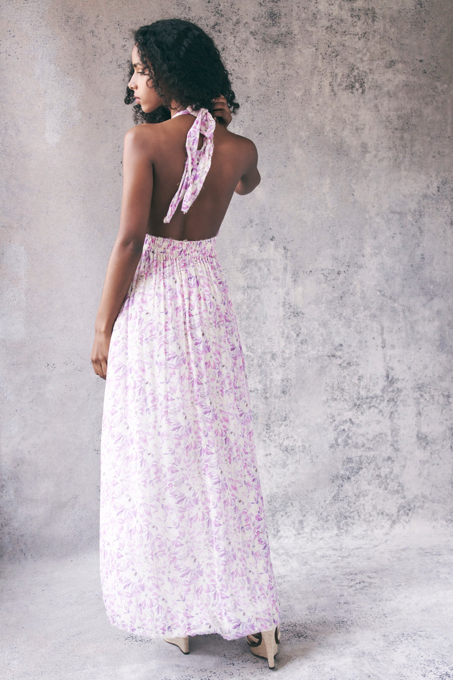 Back image of model wearing white and purple floral halter maxi dress