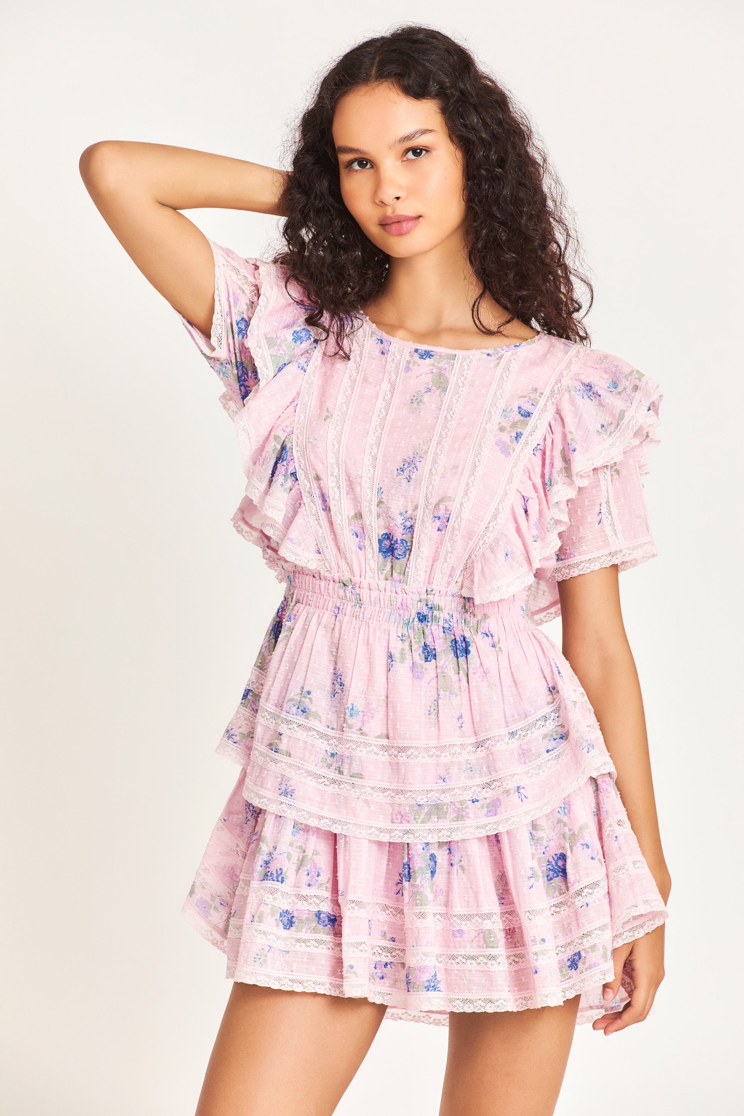 The Natasha dress in pink features double ruffled flutter sleeves, an elasticated waist, and custom lace panels at the trim of the skirt. The dress also features small blue flower prints throughout the dress. 