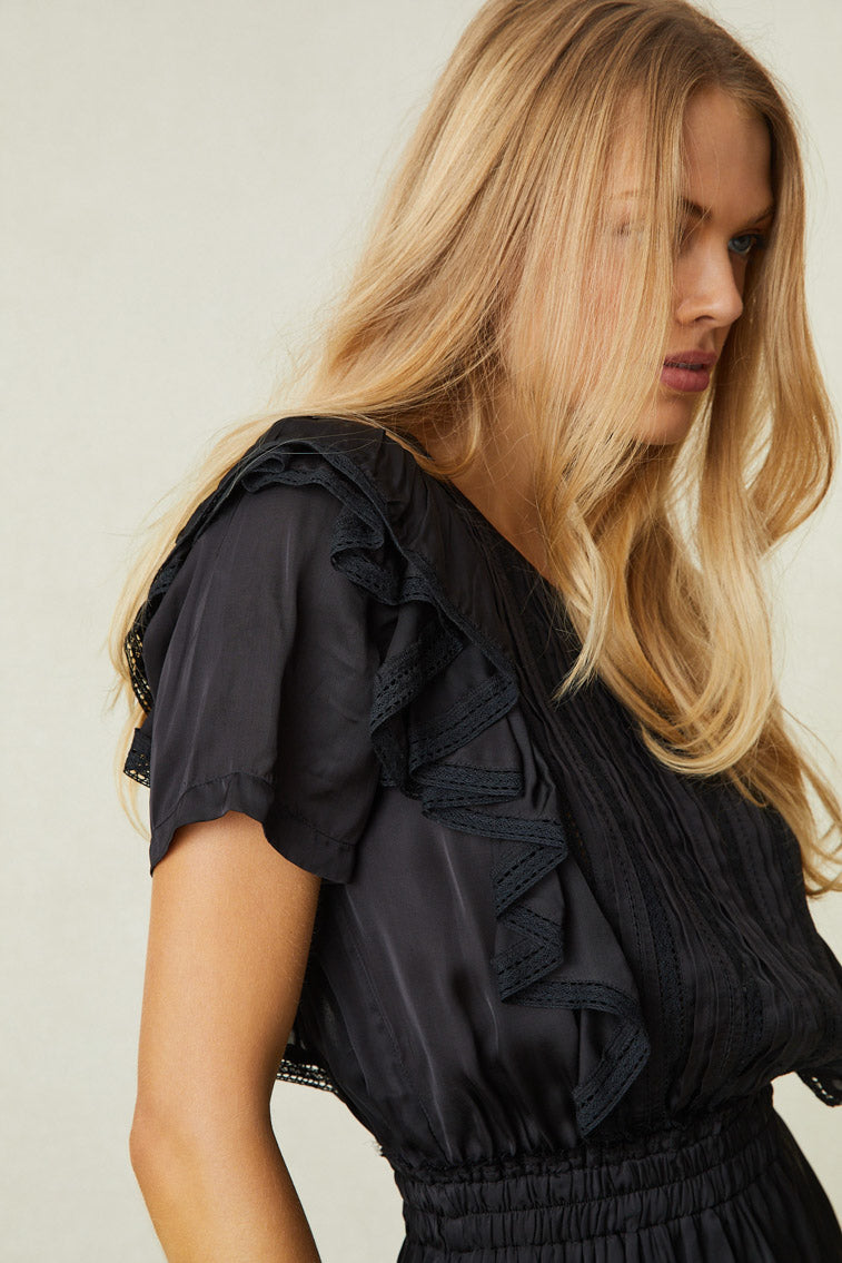 Close up image detailing ruffles on shoulder and lace on black mini dress 