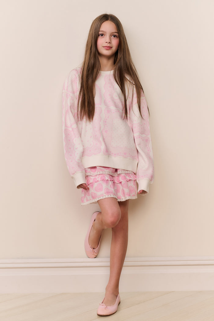 Young girl wearing a pink and white outfit against a beige wall.