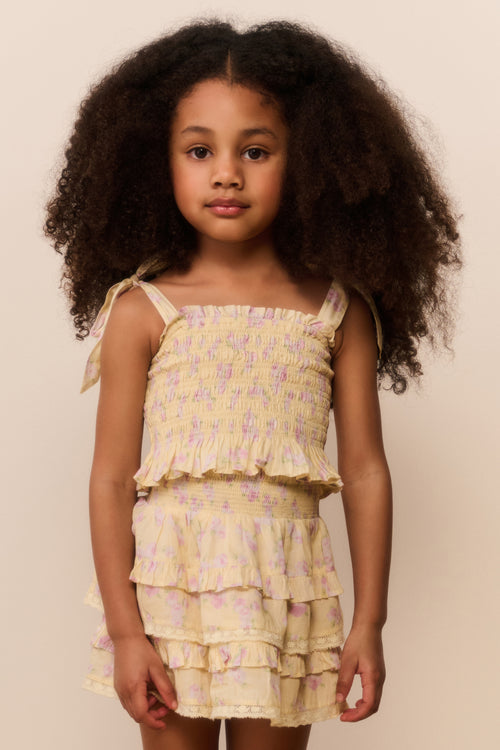 Young girl wearing a yellow floral set against a beige background