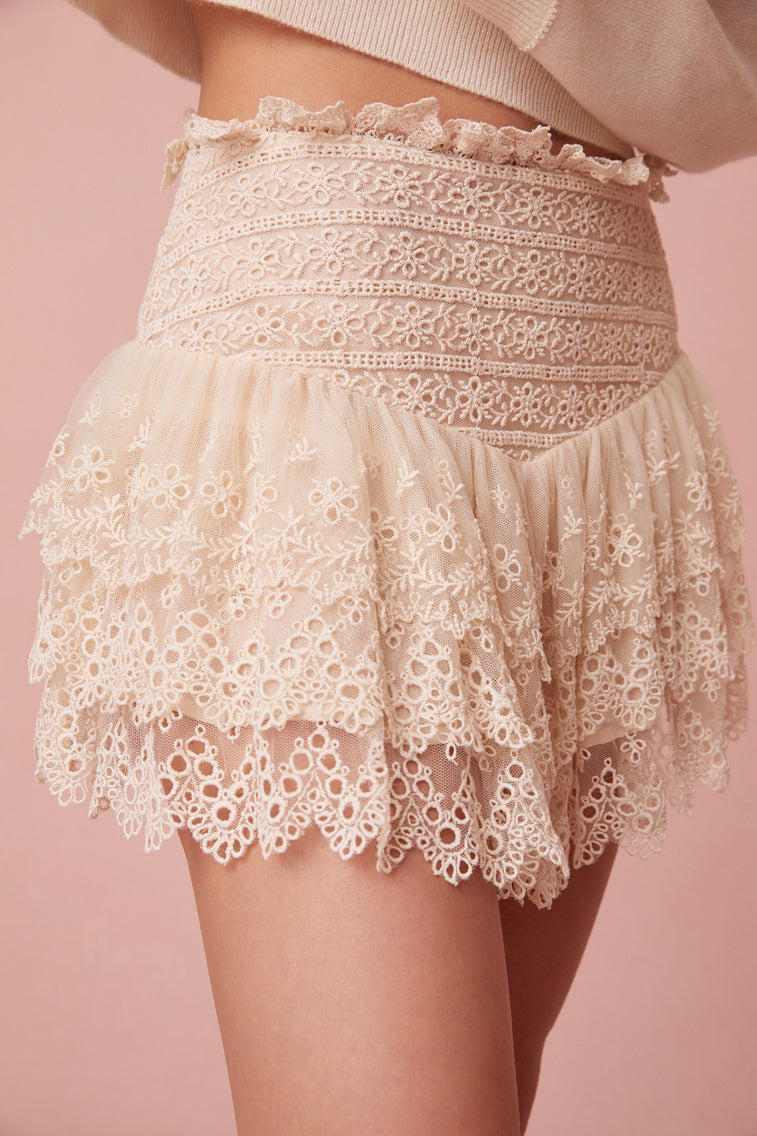 Cream mini skirt with embroidered mesh fabric. The piece has a fixed waist that hikes at the side seam and ruffles that create ethereal, dreamy tiers.