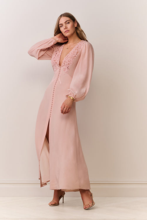 Woman wearing a long long sleeve pink dress with lace details on a plain background