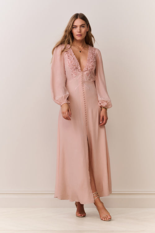 Woman wearing a long long sleeve pink dress with lace details on a plain background