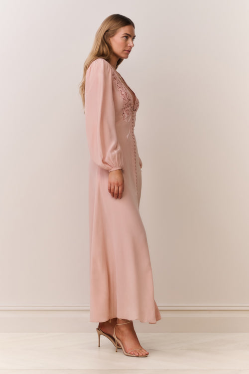 Woman wearing a long long sleeve pink dress with lace details on a plain background