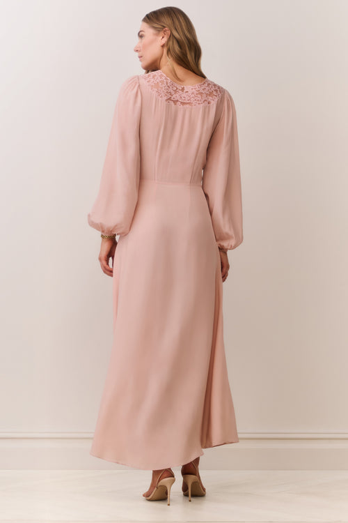 Woman wearing a long long sleeve pink dress with lace details on a plain background