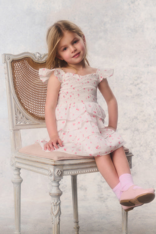 Young girl in a floral dress sitting on a chair with a white textured background