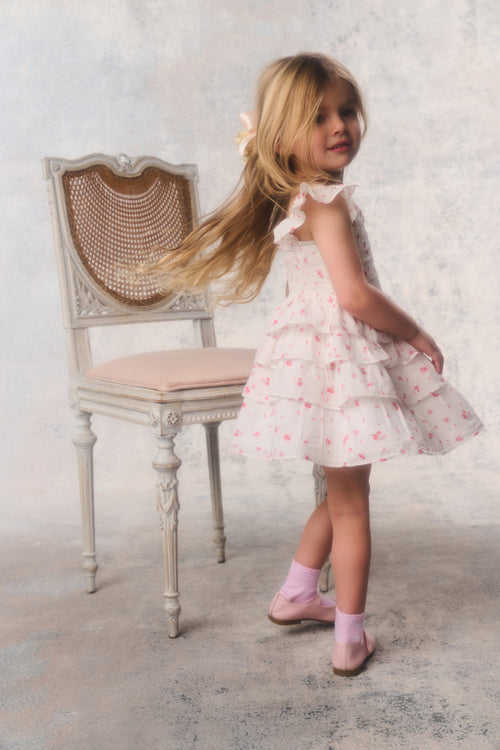Young girl in a floral dress standing next to a chair with a textured wall background