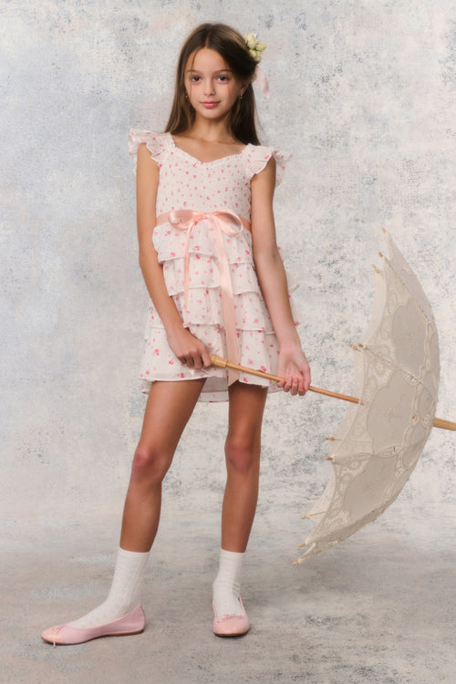 Young girl in a light dress holding an umbrella against a textured wall.