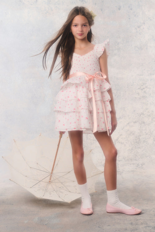 Young girl in a white dress with pink accents holding an umbrella against a light background