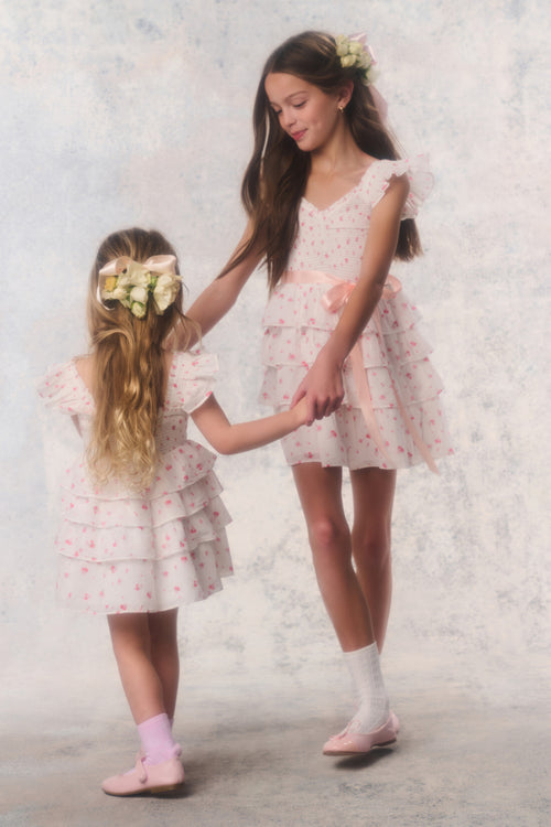 Two young girls in matching floral dresses standing against a light background