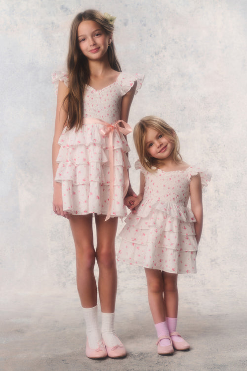 Two young girls wearing matching floral dresses against a light background