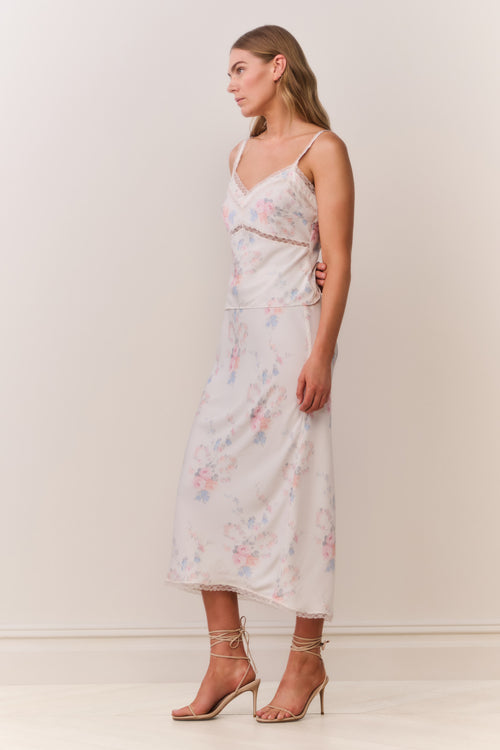 Woman wearing a floral satin lace trim camisole with thin straps and matching skirt on a plain background