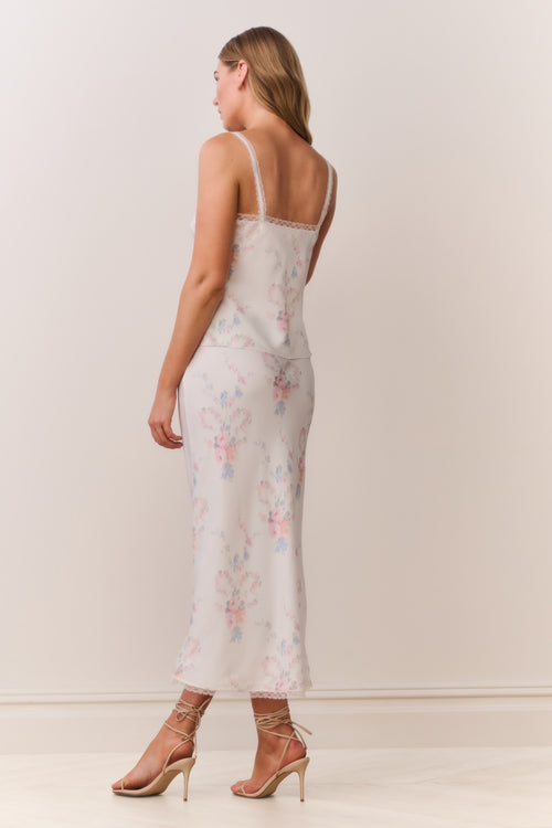 Woman wearing a floral satin lace trim camisole with thin straps and matching skirt on a plain background