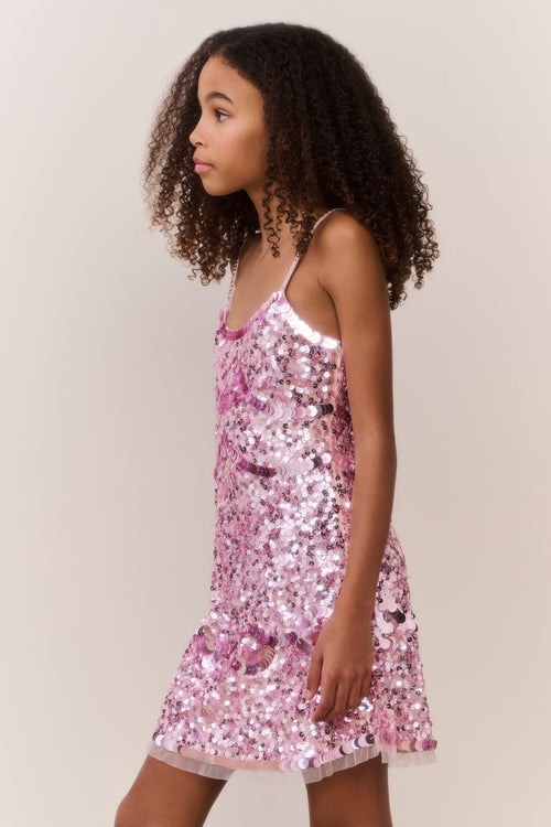 Young girl wearing a pink sequin dress against a plain background