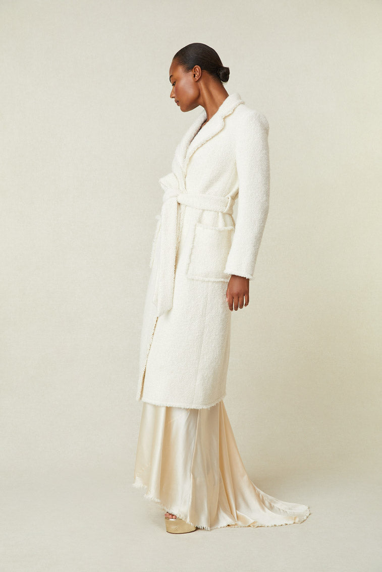 Model wearing midi length coat with waist tie and pockets.