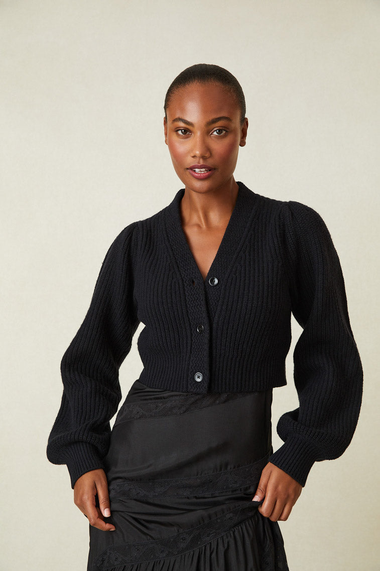 Black cashmere-wool blend cropped sweater, has a v-neck that descends to three buttons at center front. Pleated blouson sleeves extend to ribbed cuffs at opening.