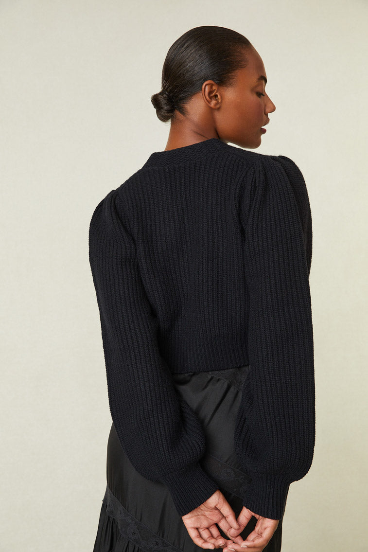 Back of cropped Black cashmere-wool blend cropped sweater, has a v-neck that descends to three buttons at center front. Pleated blouson sleeves extend to ribbed cuffs at opening.
