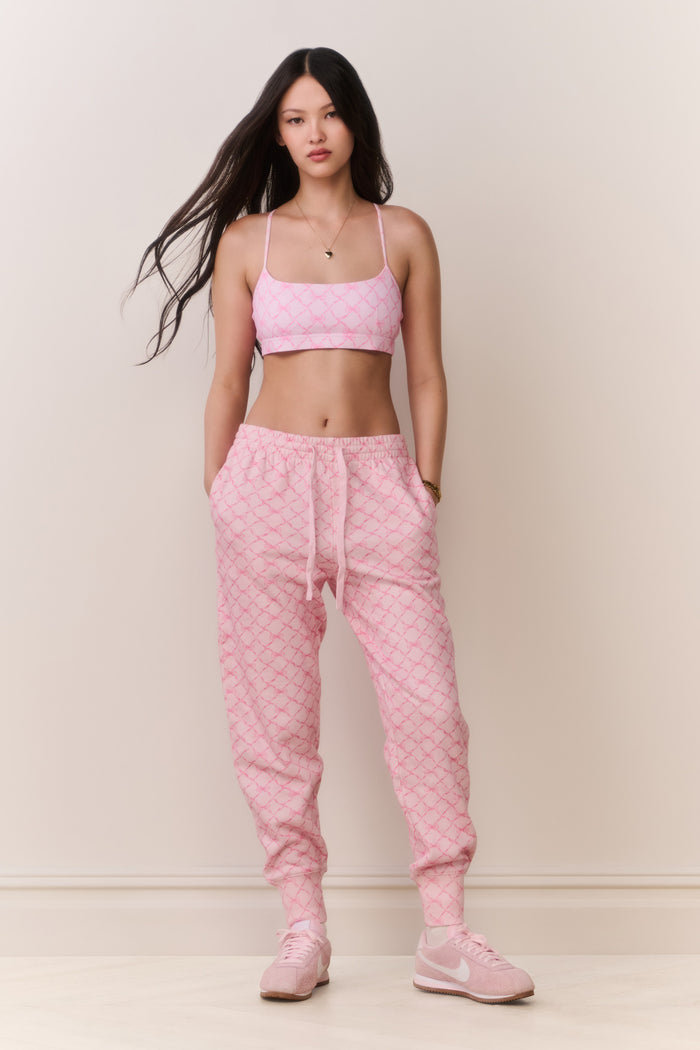 Woman wearing a pink bow print sports bra and matching sweatpants set on a plain background