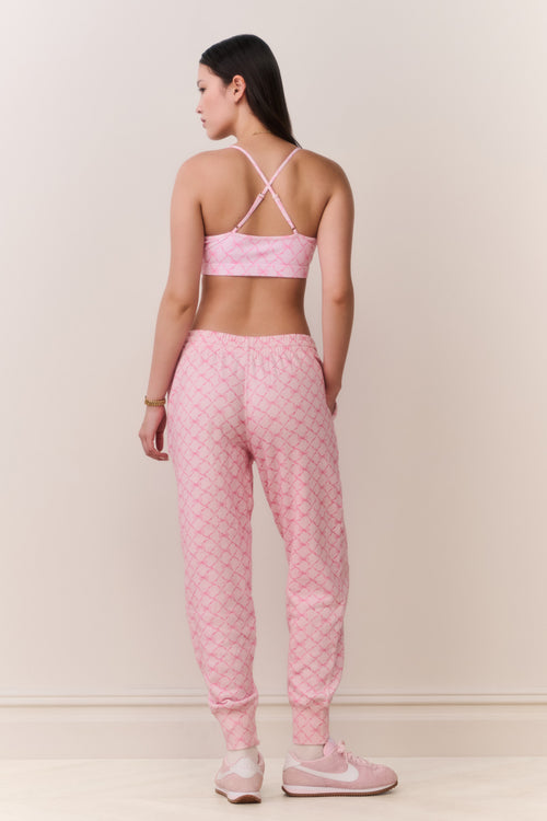 Woman wearing a pink bow print sports bra and matching sweatpants set on a plain background