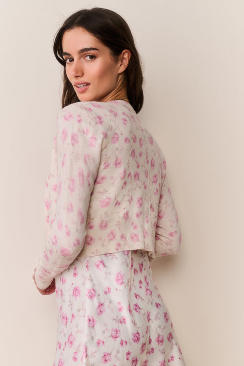 Woman wearing a light-colored floral cardigan and matching dress against a plain background