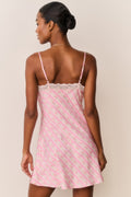 Woman wearing a pink patterned slip dress against a plain background