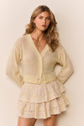 Woman wearing a pale yellow-colored cardigan over a patterned ruffle skirt on a plain background