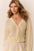 Woman wearing a pale yellow-colored cardigan over a patterned ruffle skirt on a plain background