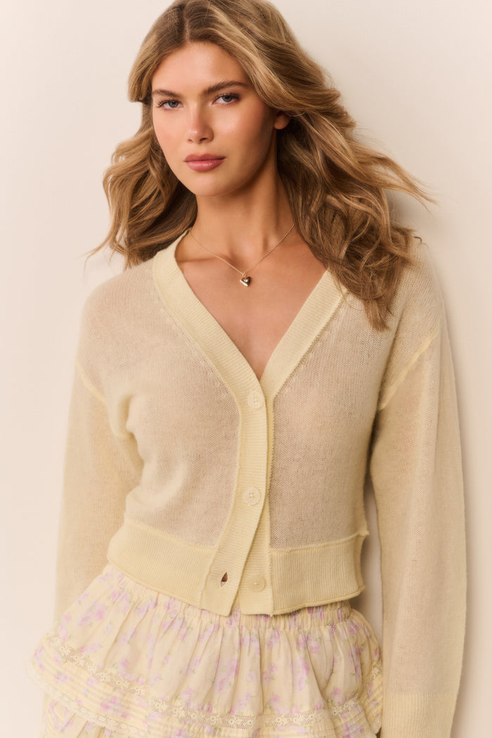 Woman wearing a pale yellow-colored cardigan over a patterned ruffle skirt on a plain background