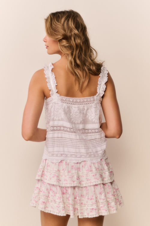 Woman wearing a white lace sleeveless top with a floral tiered ruffle mini skirt on a beige background