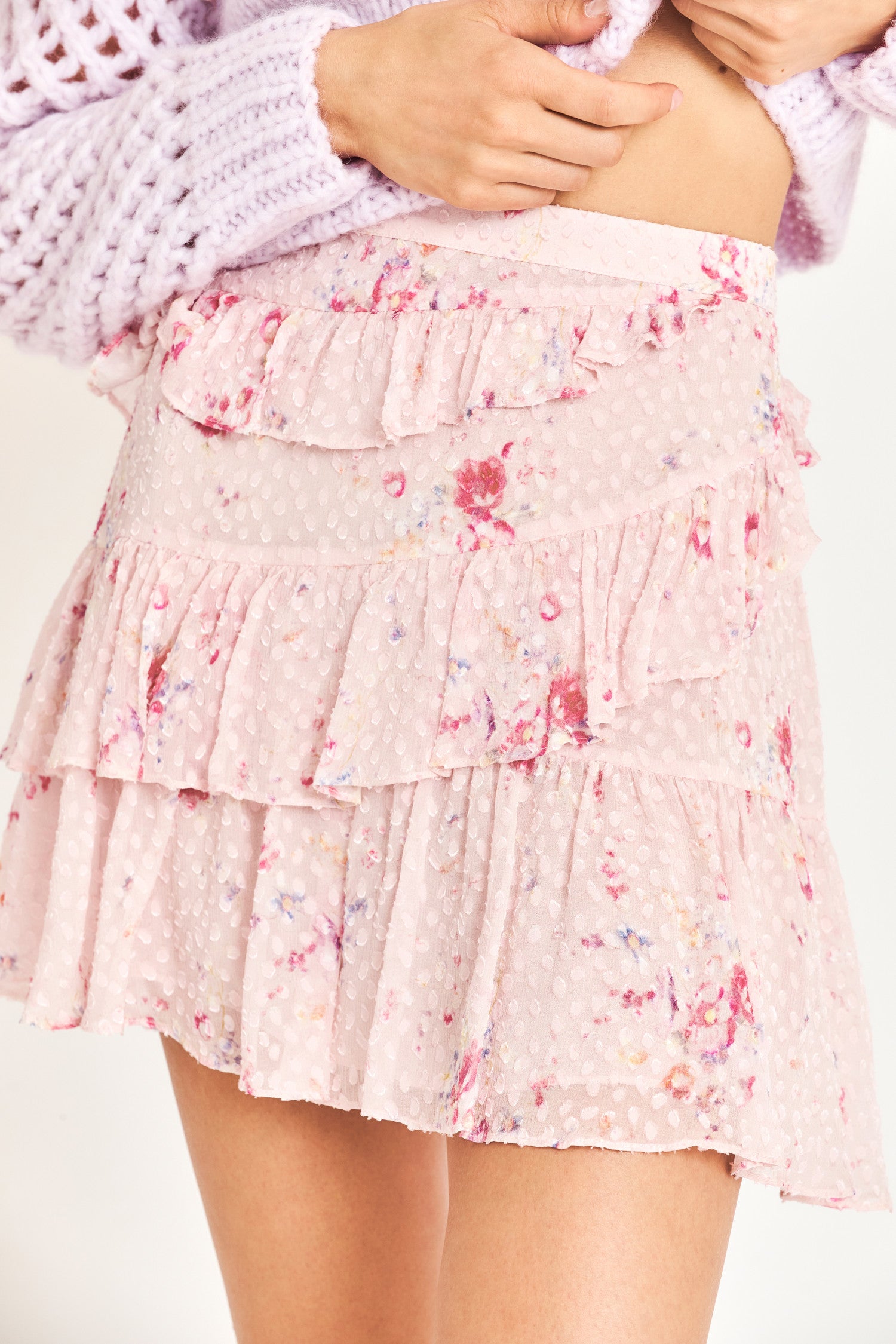 Close up image detailing ruffles and floral print on pink mini skirt