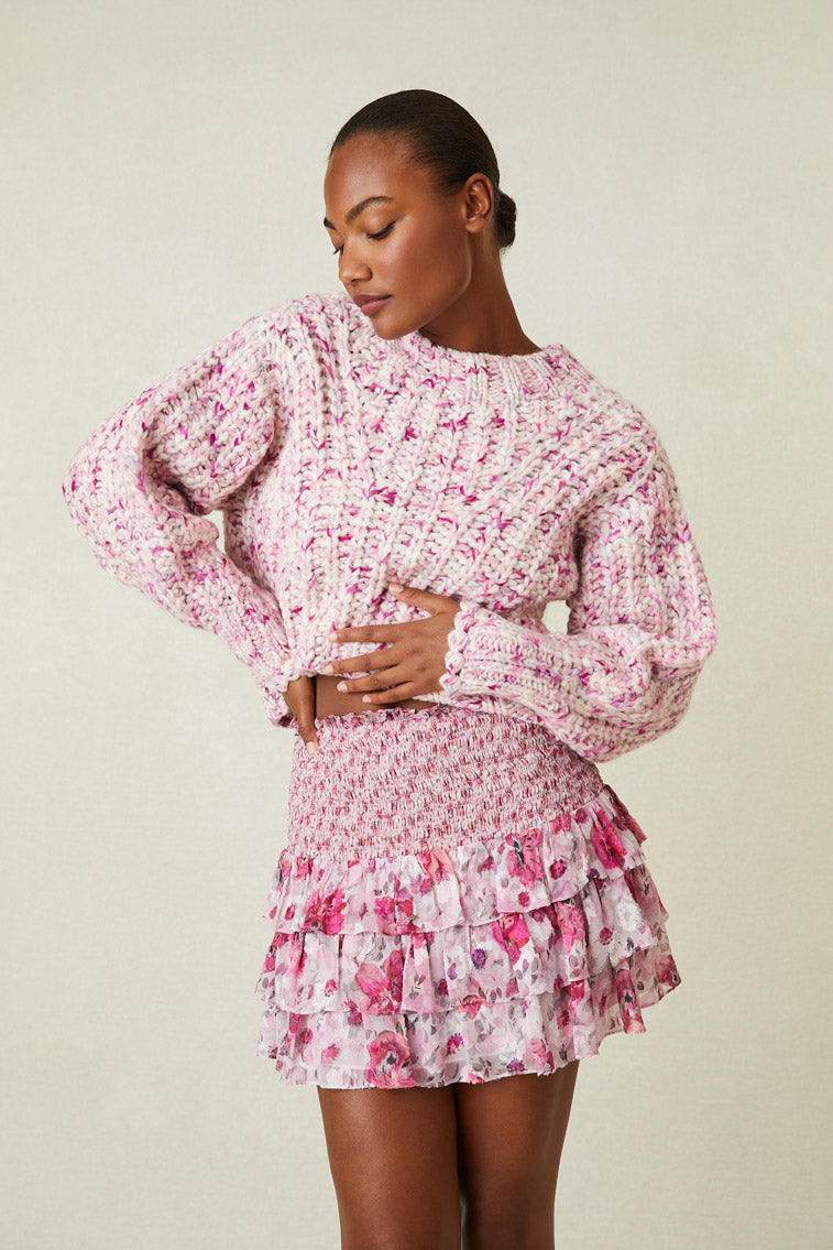 Model wearing pink multi print mini skirt with smocked waistband and ruffle bottom.
