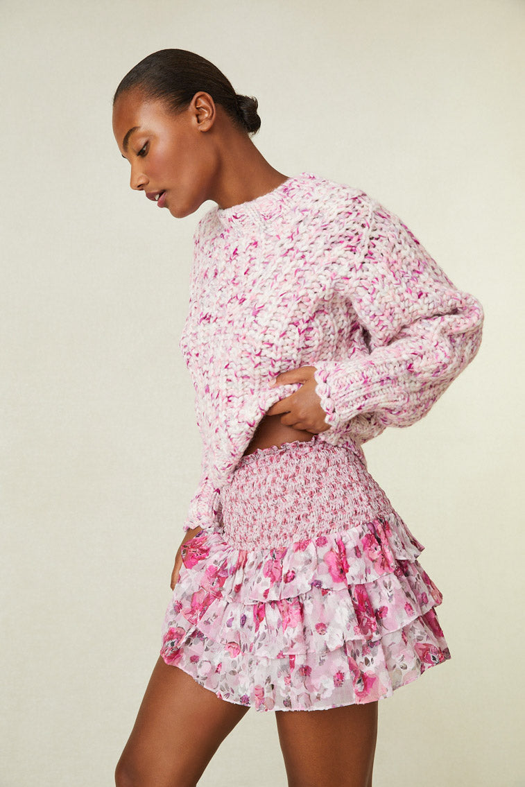 Side image of model wearing pink multi print mini skirt with smocked waistband and ruffle bottom.