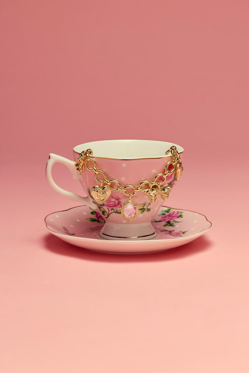Teacup and saucer with a gold bracelet on a pink background