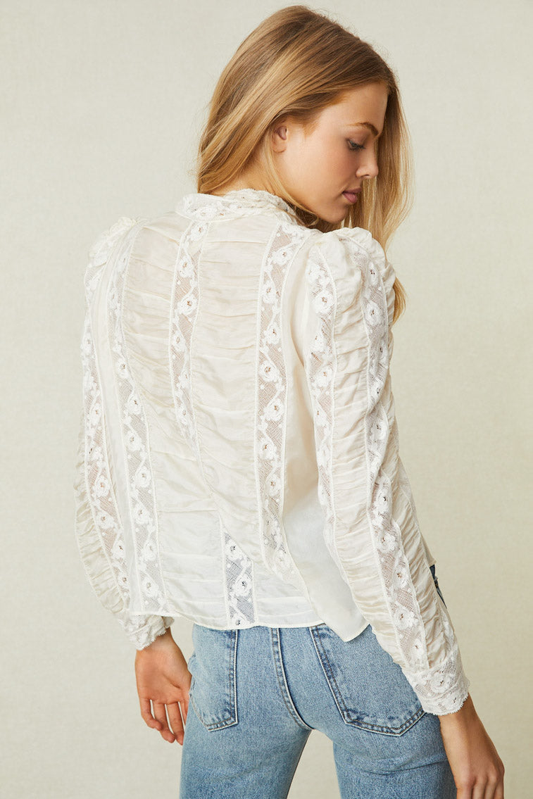 Back image of model wearing white long sleeve blouse with lace panels and puff shoulders. 