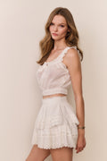 Woman wearing a white lace top and skirt set against a beige background