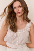 Woman wearing a white sleeveless top with lace details against a plain background