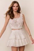 Woman wearing a white lace top and skirt set against a plain background