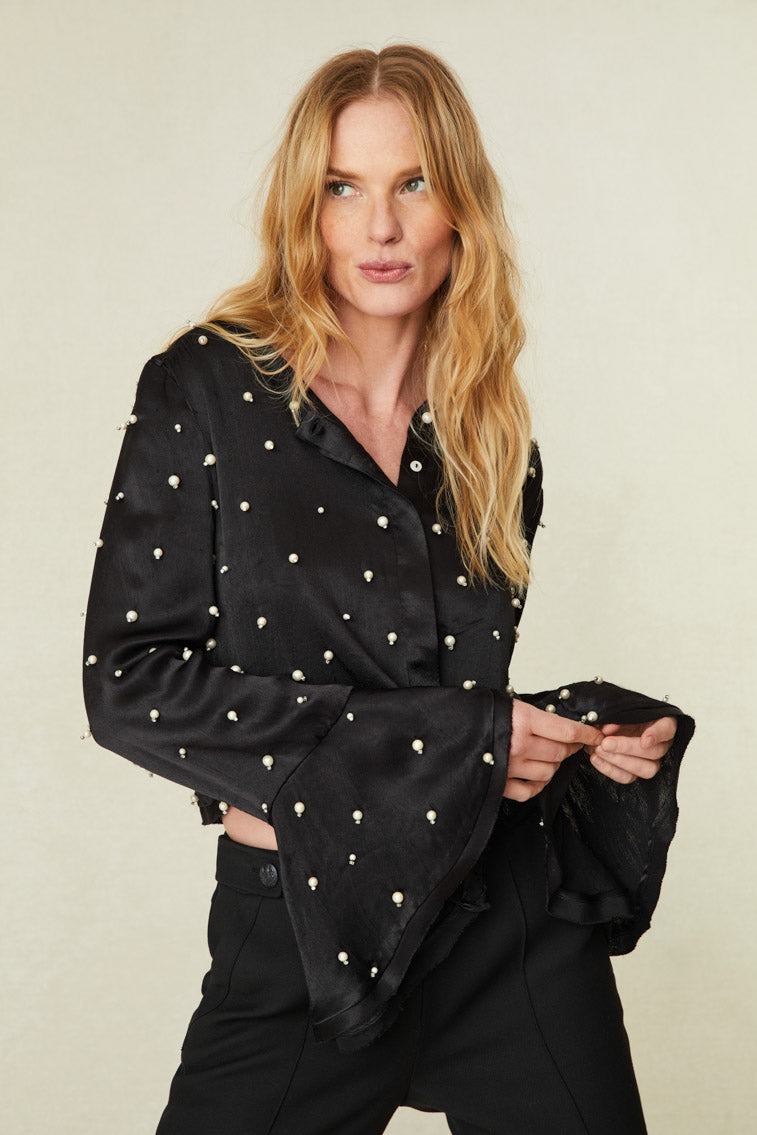 adorned with iridescent pearl embellishments all over. The button-up top arrives slightly cropped with long sleeves that have a wide opening at the cuff for bell-like shape. Raw edge and fraying detail lines the sleeve openings and the hem.