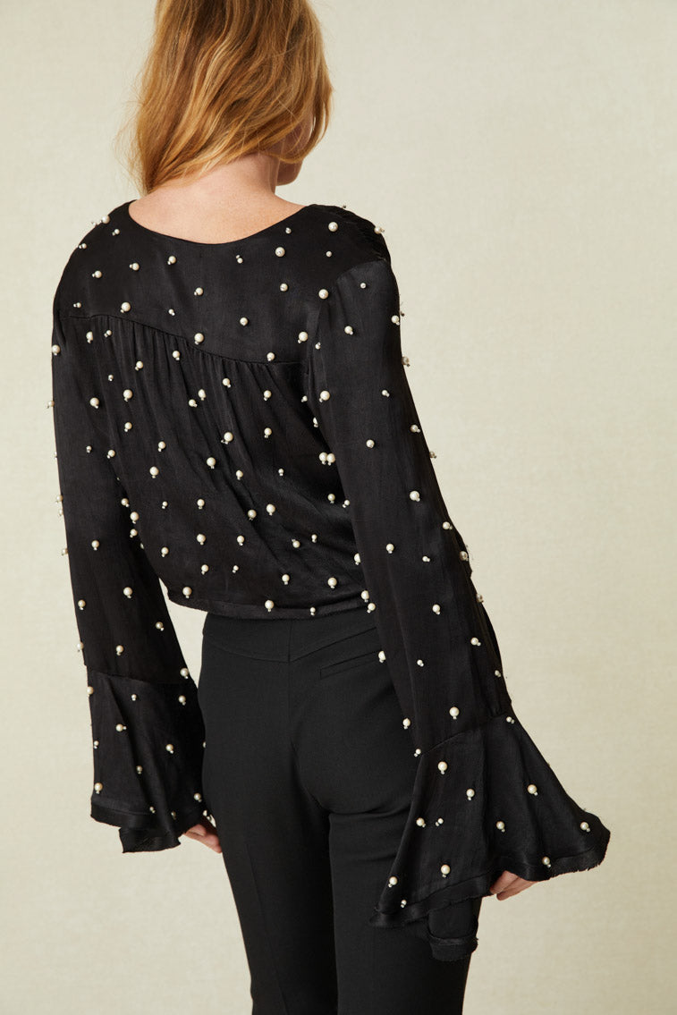 adorned with iridescent pearl embellishments all over. The button-up top arrives slightly cropped with long sleeves that have a wide opening at the cuff for bell-like shape. Raw edge and fraying detail lines the sleeve openings and the hem.