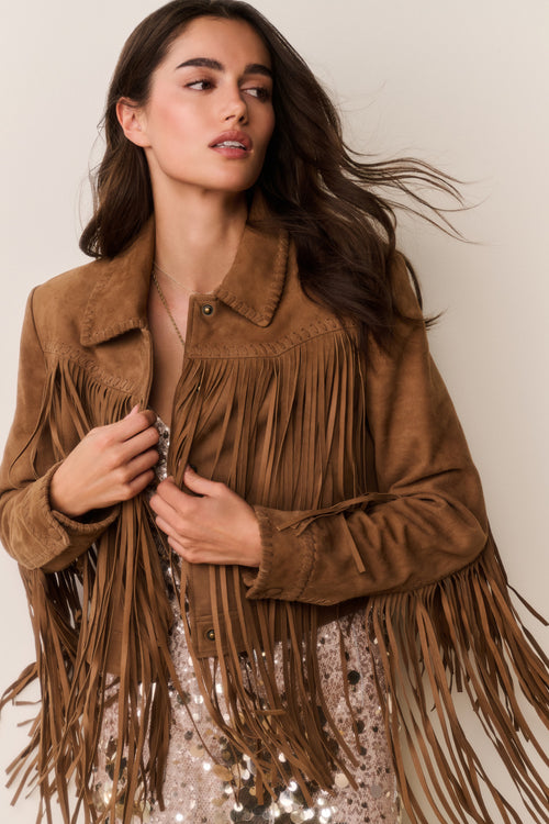 Woman wearing a brown suede fringed jacket and gold sequin dress with a plain background