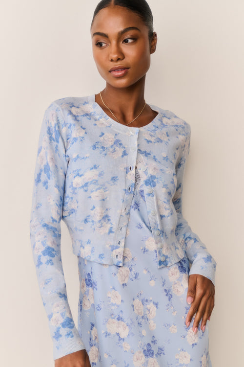 Woman wearing a light blue floral cardigan over a matching dress against a beige background