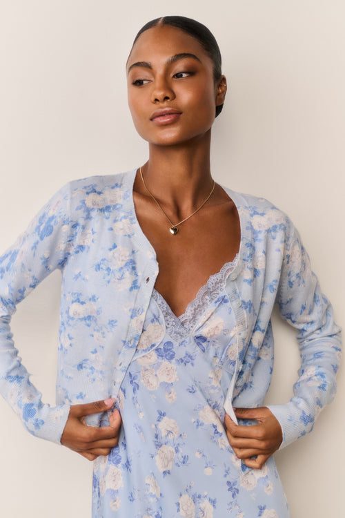Woman wearing a light blue floral cardigan over a matching dress against a plain background