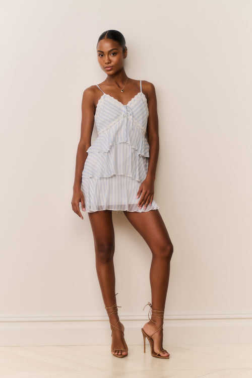 Woman wearing White and blue striped and tiered mini dress against a plain background