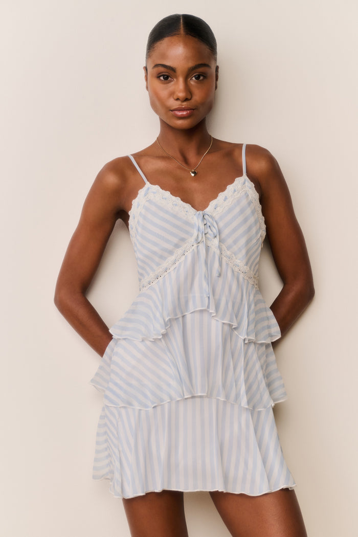 Woman wearing White and blue striped and tiered mini dress against a plain background