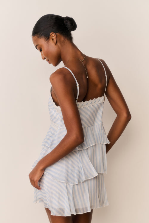 Woman wearing White and blue striped and tiered mini dress against a plain background